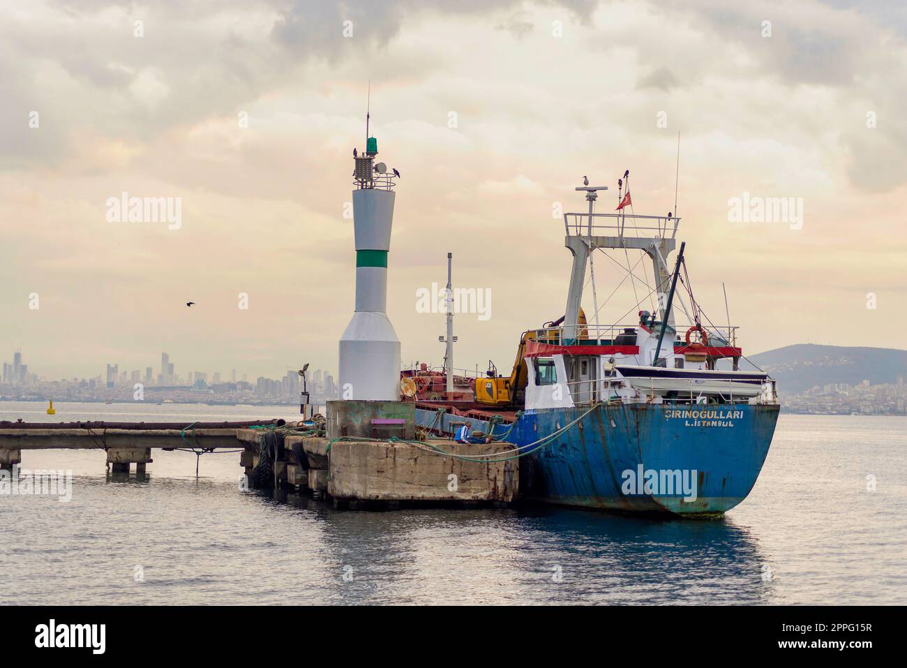 Nave da carico ormeggiata accanto a un piccolo faro, al porto dell'isola di Kinaliada, nel mare di Marmara, vicino a Istanbul, in Turchia, all'ora dell'alba Foto Stock