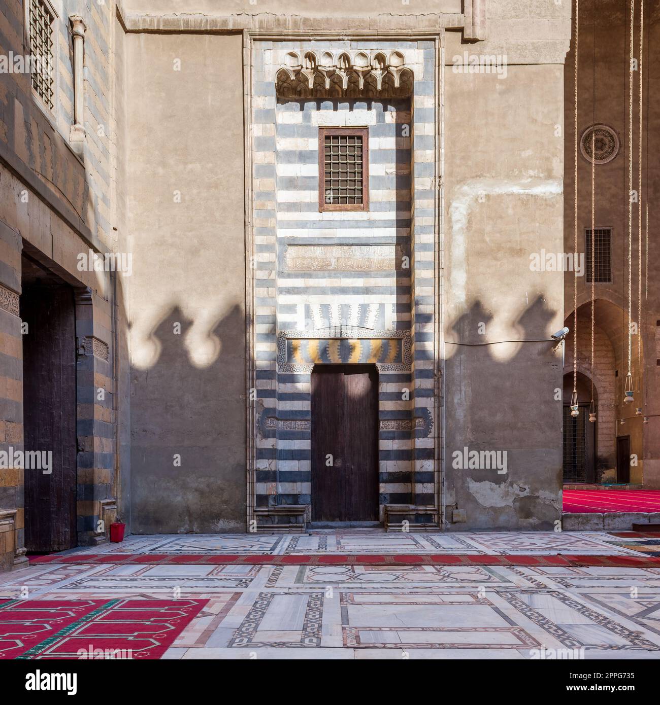Parete con decorazioni in marmo bianco e nero a righe, porta e finestra grunge in legno, moschea Sultan Hassan, Cairo, Egitto Foto Stock