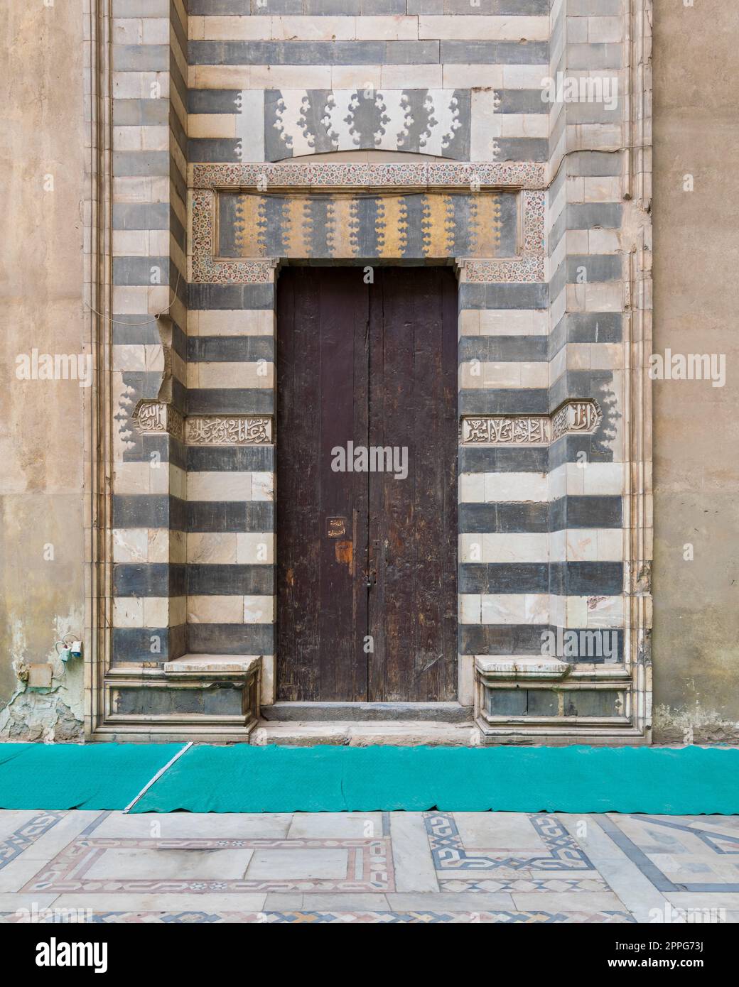 Porta in legno invecchiata circondata da decorazioni in marmo bianco e nero a righe, Moschea Sultan Hassan, Cairo, Egitto Foto Stock