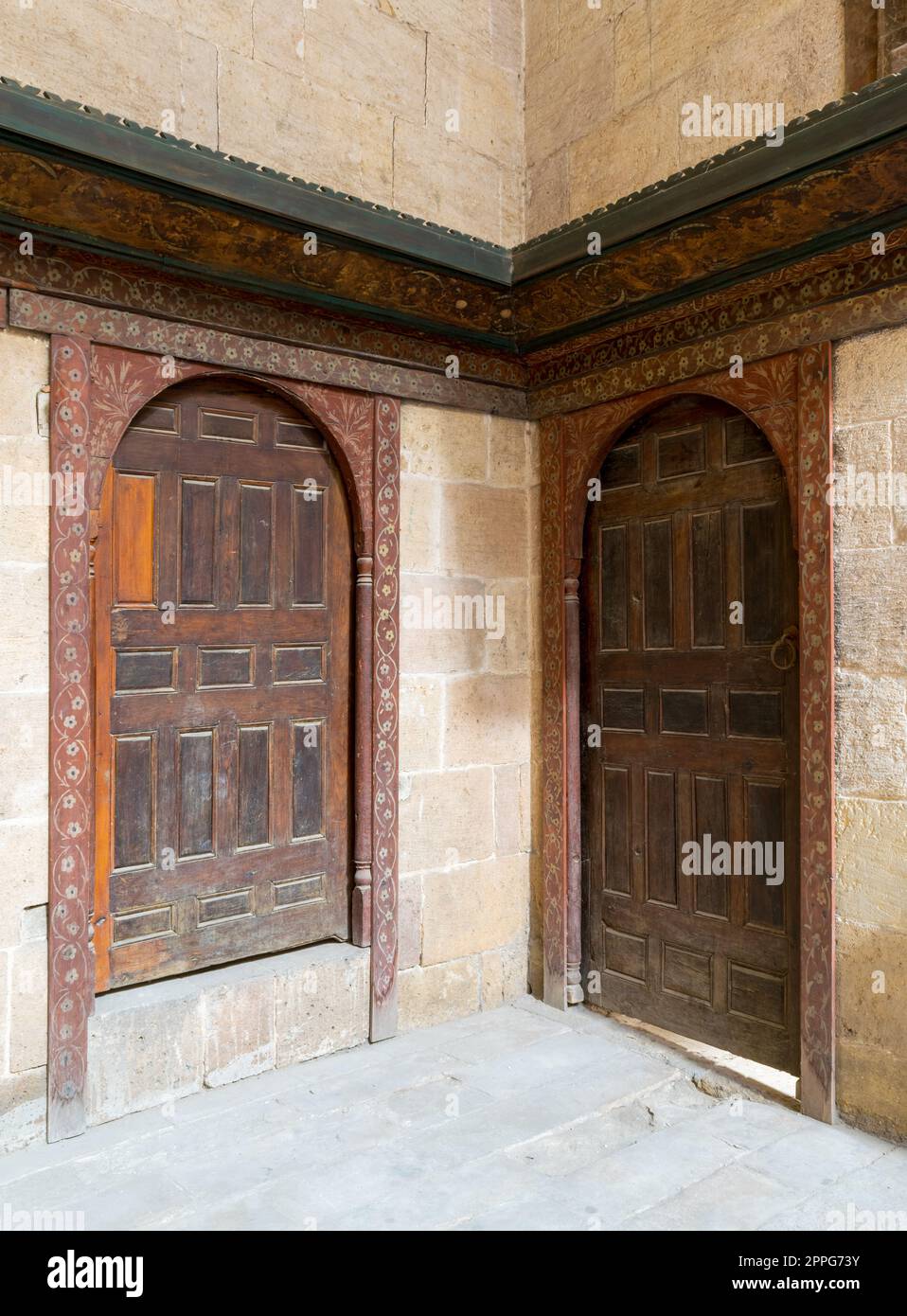 Due porte perpendicolari a volta ornate in legno invecchiate su pareti in mattoni di pietra Foto Stock