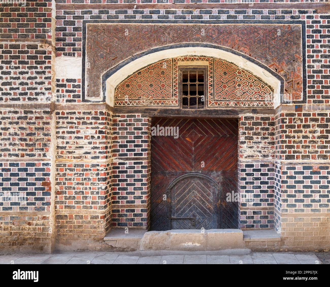 Cancello ad arco decorato in legno grunge con piccola porta interna a parete con mattoni neri e rossi Foto Stock