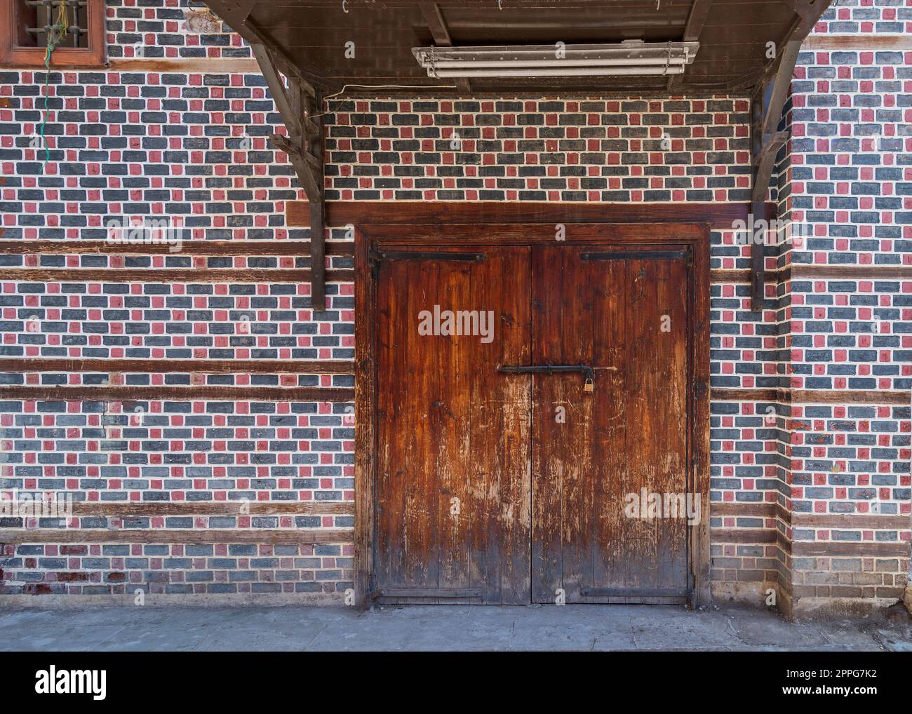 Grunge porta d'ingresso ad arco decorata in legno con baldacchino in legno sopra al muro con mattoni neri e rossi con cuciture bianche Foto Stock