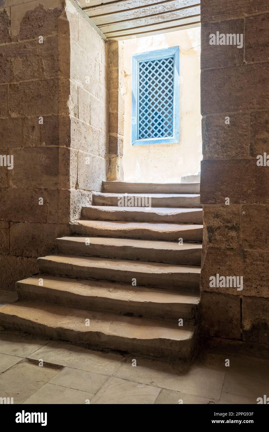 Vecchio stretto passaggio scuro e scalinata che porta alla piccola lobby esterna con finestre di legno blu Foto Stock