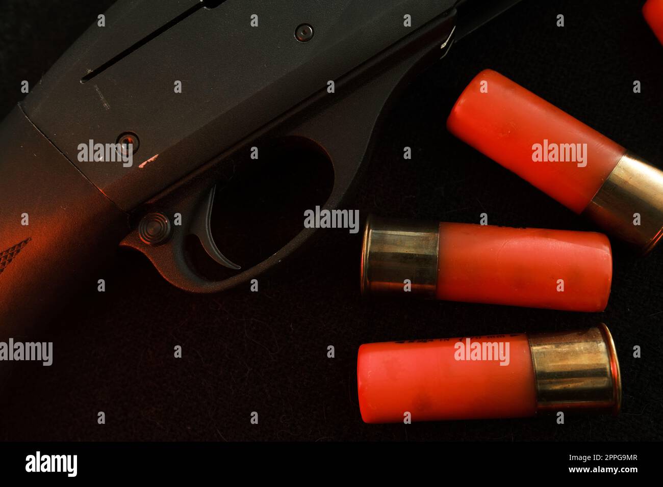 Grilletto di un fucile su sfondo nero con fulmine rosso con proiettili Shotgun su una superficie nera. Munizioni per armi a foro liscio da 12 gauge. Caccia alle munizioni. Sfondo scuro. Foto Stock