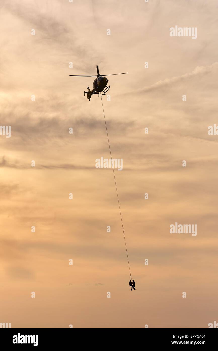 Elicottero di salvataggio che trasporta persone ferite appese su una corda Foto Stock