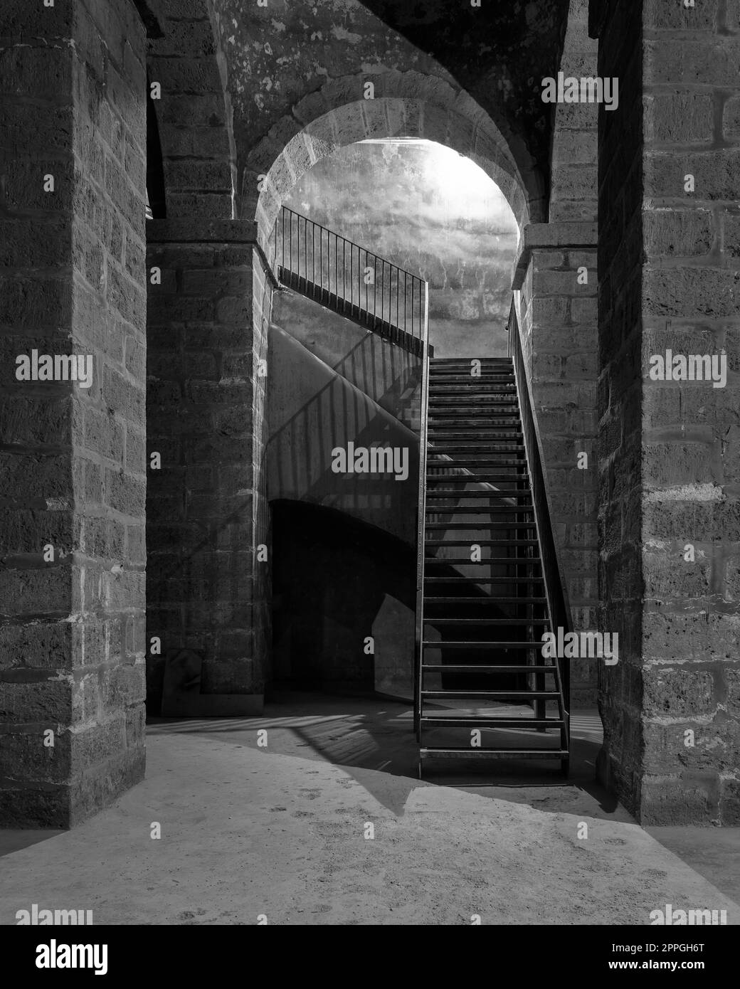 Bianco e nero di passaggio sotterraneo abbandonato scuro con colonne in mattoni di pietra e scale in metallo Foto Stock