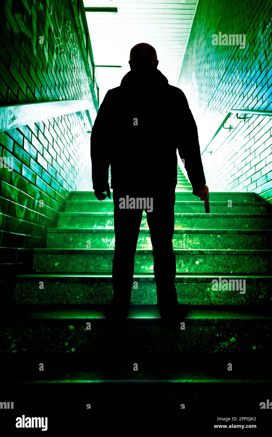 uomo misterioso e minaccioso in piedi sulle scale con una pistola in mano Foto Stock