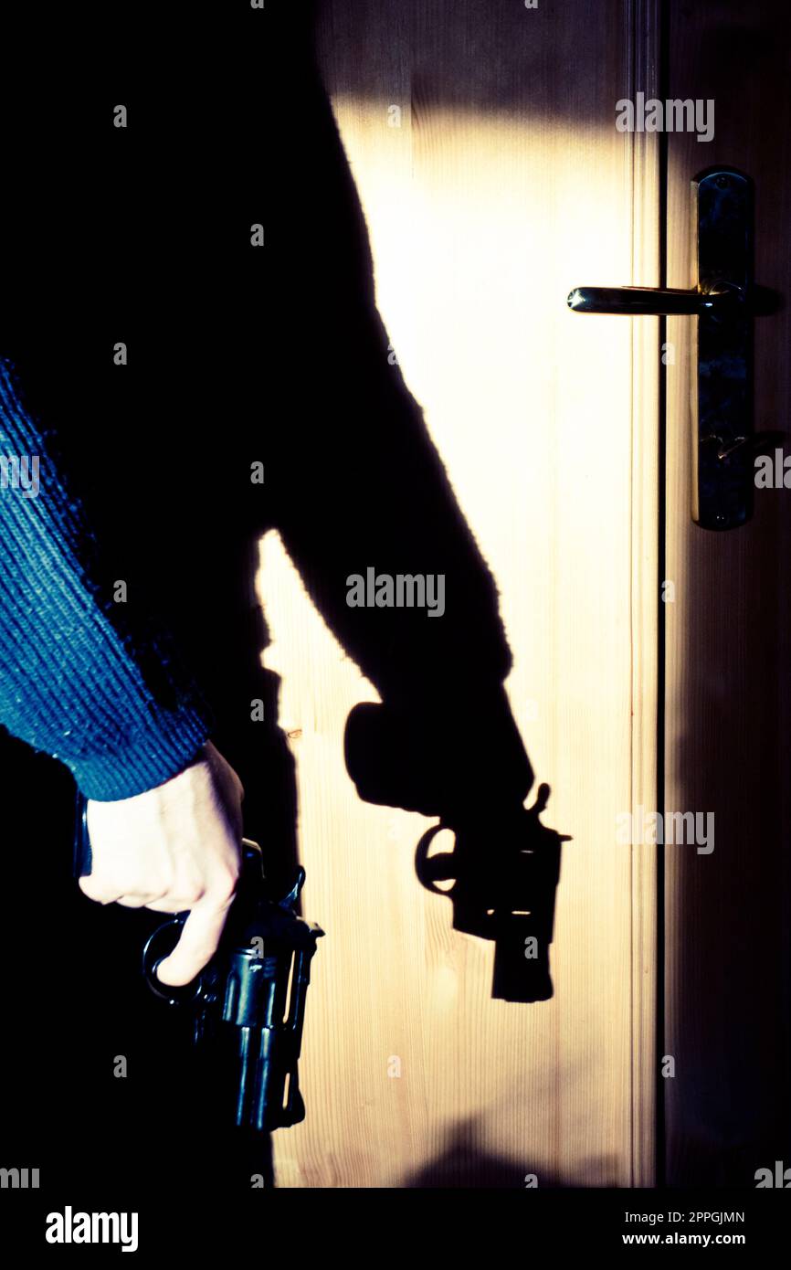uomo misterioso che tiene una pistola, ombra proiettata su una porta Foto Stock