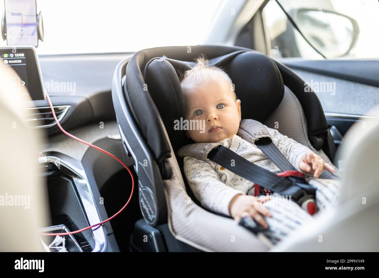 Bambino tenero legato al seggiolino per auto nell'abitacolo durante la guida dell'auto. Foto Stock