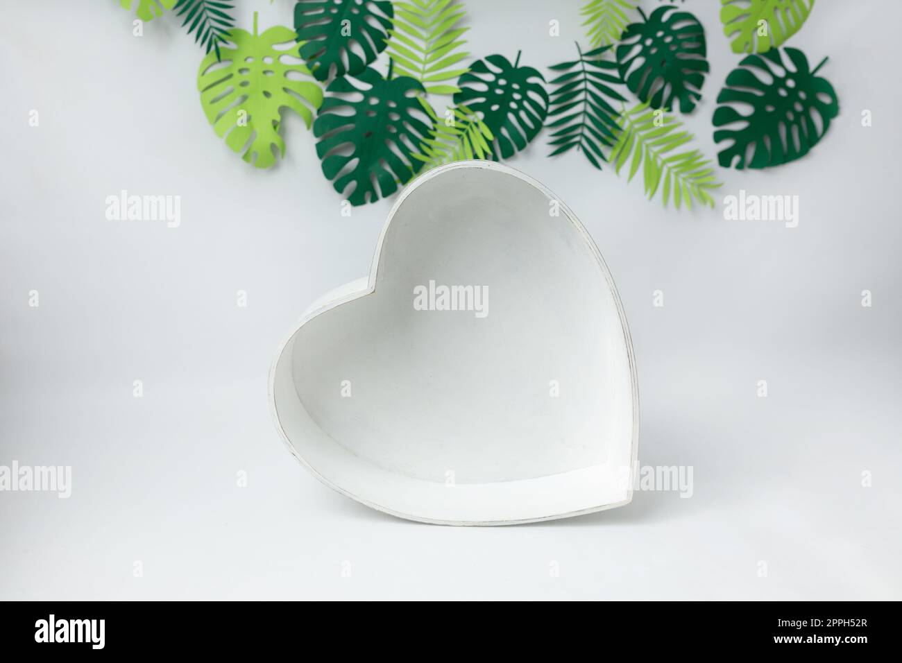 cuore in legno su fondo bianco con foglie verdi. cestino per fotografia neonato. foglie. cuore Foto Stock