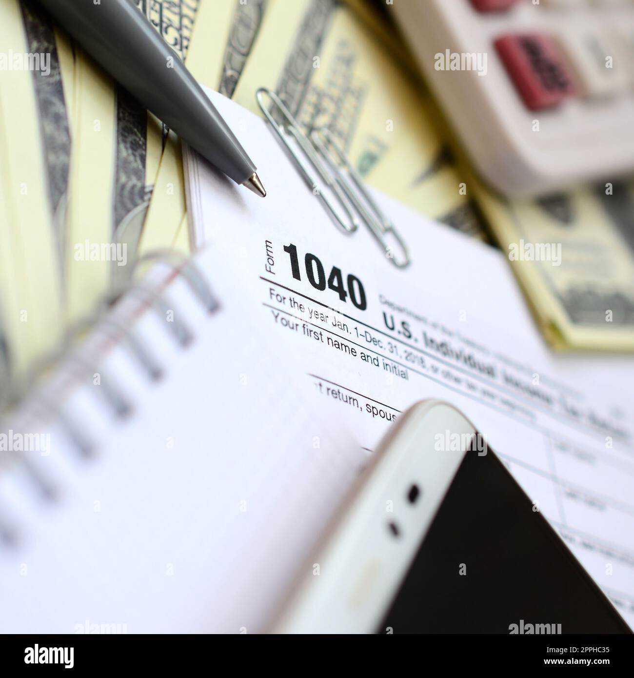 La penna, il notebook, la calcolatrice, lo smartphone e le fatture del dollaro si trova sul modulo di imposta 1040 US Reddito Individuale ritorno di imposta. Il tempo di pagare le tasse Foto Stock