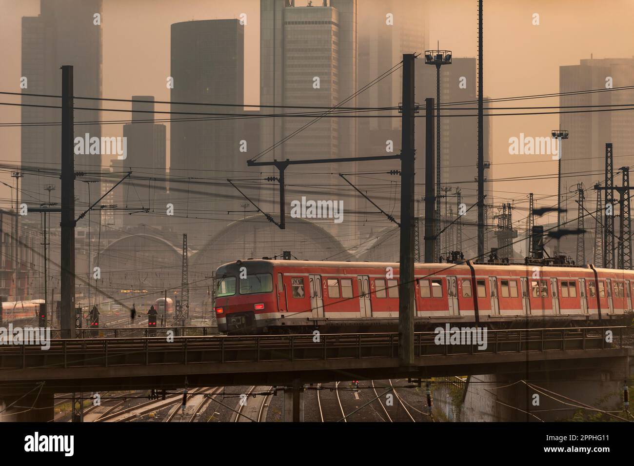 Un treno cittadino passa nella foschia mattutina o alla luce serale di fronte allo skyline dei grattacieli di Francoforte sul meno, in piedi nella nebbia Foto Stock