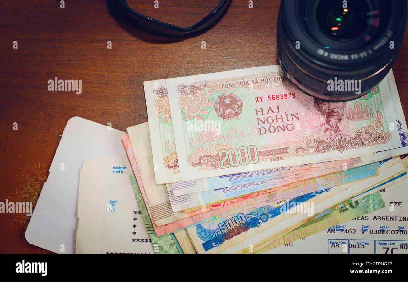 Obiettivo per fotocamera, denaro straniero e carta d'imbarco per aerei su un tavolo di legno. Attrezzature per turismo, vacanza, fotografia di viaggio. Foto Stock