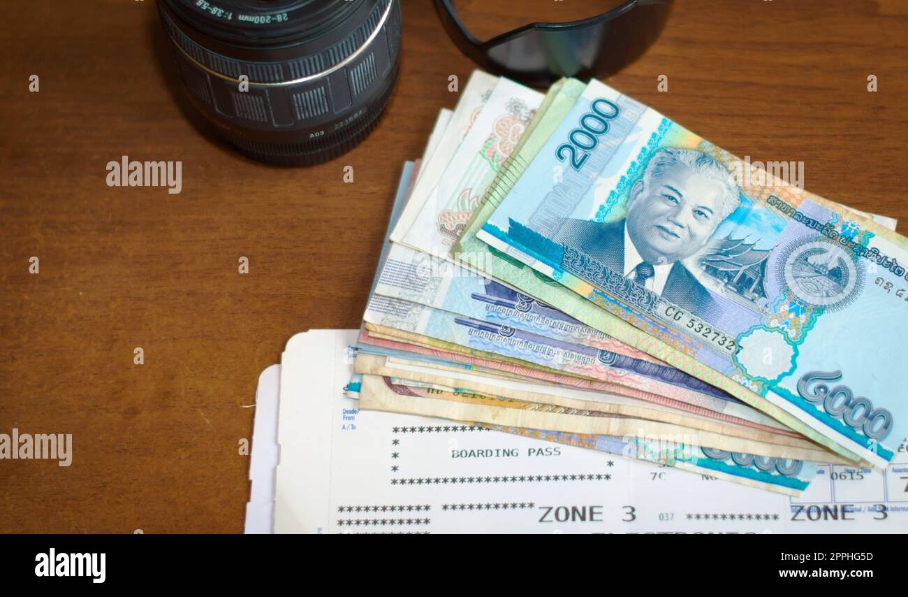 Obiettivo per fotocamera, denaro straniero e carta d'imbarco per aerei su un tavolo di legno. Attrezzature per turismo, vacanza, fotografia di viaggio. Foto Stock