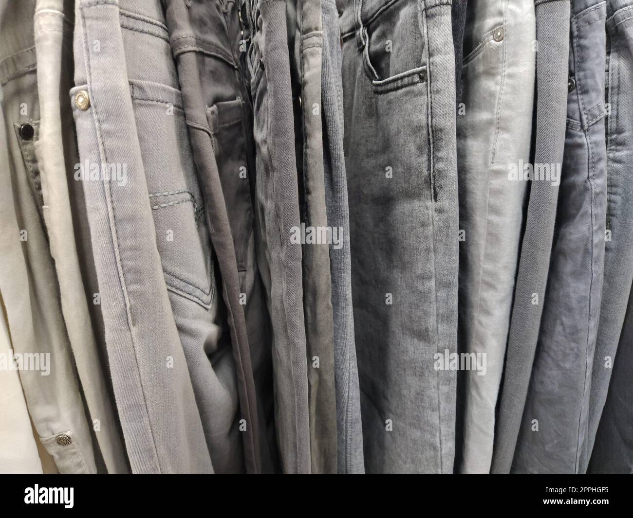 Vestiti appesi agli appendiabiti. Assortimento di articoli di seconda mano. Abiti appesi a un rack, pronti per la vendita ai clienti. Risparmiare denaro in crisi. Shopping economico. Jeans e pantaloni. Foto Stock
