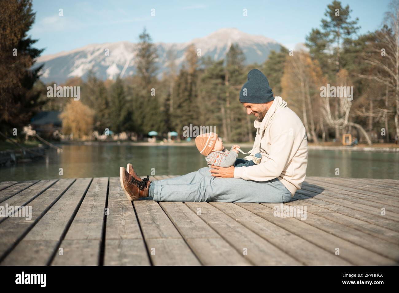 Famiglia felice. Padre che gioca con il suo bambino oudoors nella soleggiata giornata autunnale. Ritratto di papà e figlio piccolo su una piattaforma di legno vicino al lago. Emozioni positive, sentimenti, gioia. Foto Stock