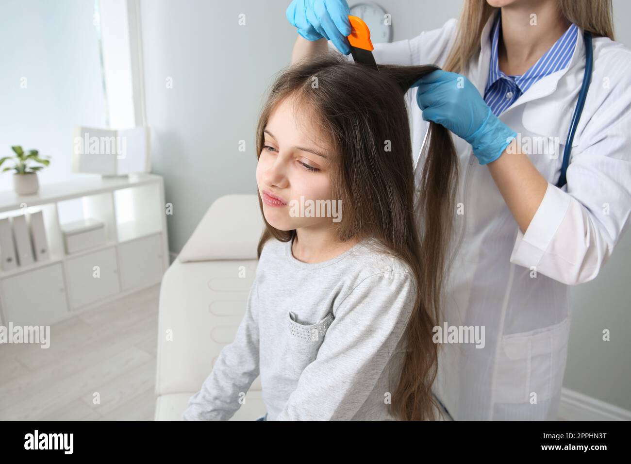 Medico che usa il pettine nit sui capelli della ragazza in clinica. Trattamento antighiaccio Foto Stock