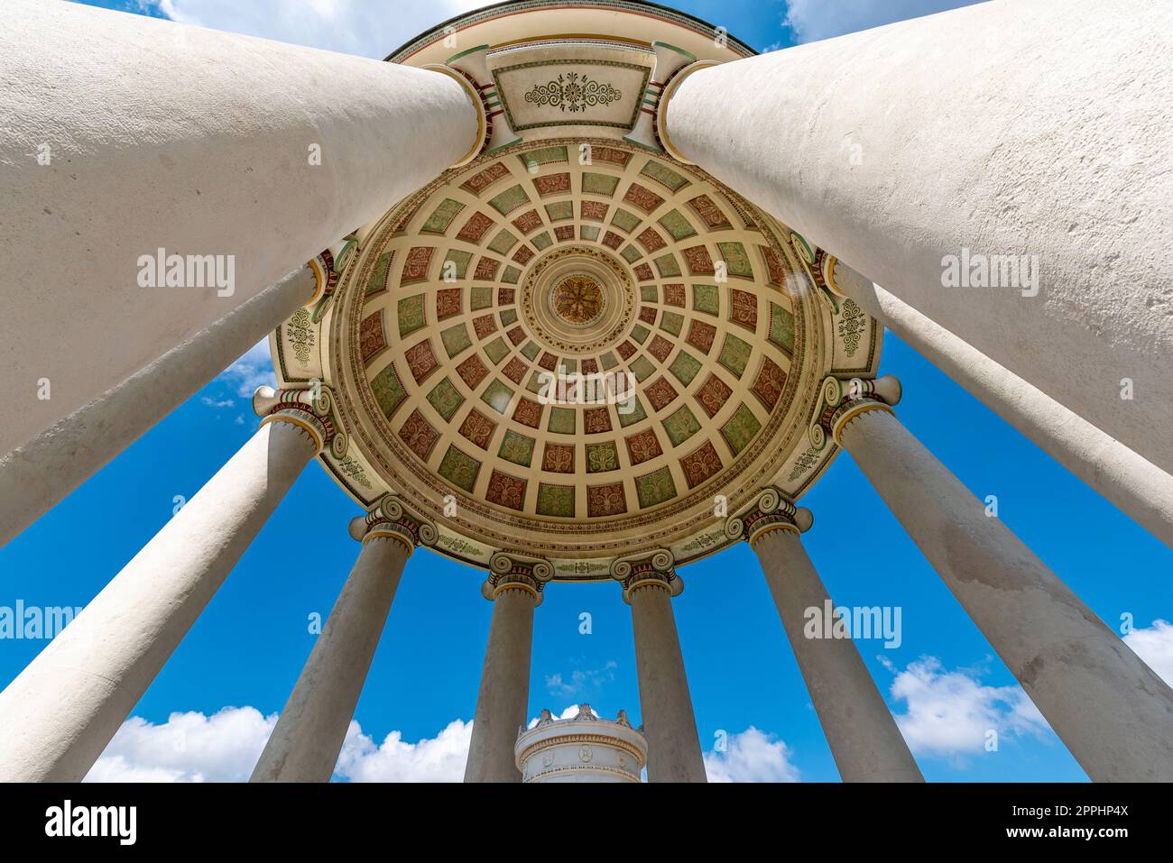 La cupola e le colonne del tempio monoptero nel giardino inglese di Monaco di Baviera con un grandangolo estremo girato dal basso, sotto il cielo blu e la copertura di nuvole di luce Foto Stock