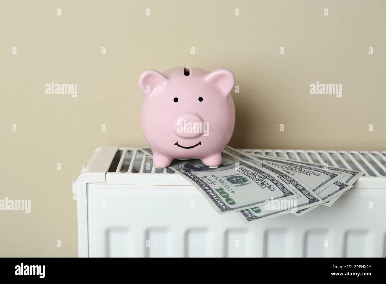 La banca del piggy e le banconote del dollaro sul radiatore di riscaldamento contro lo sfondo beige Foto Stock