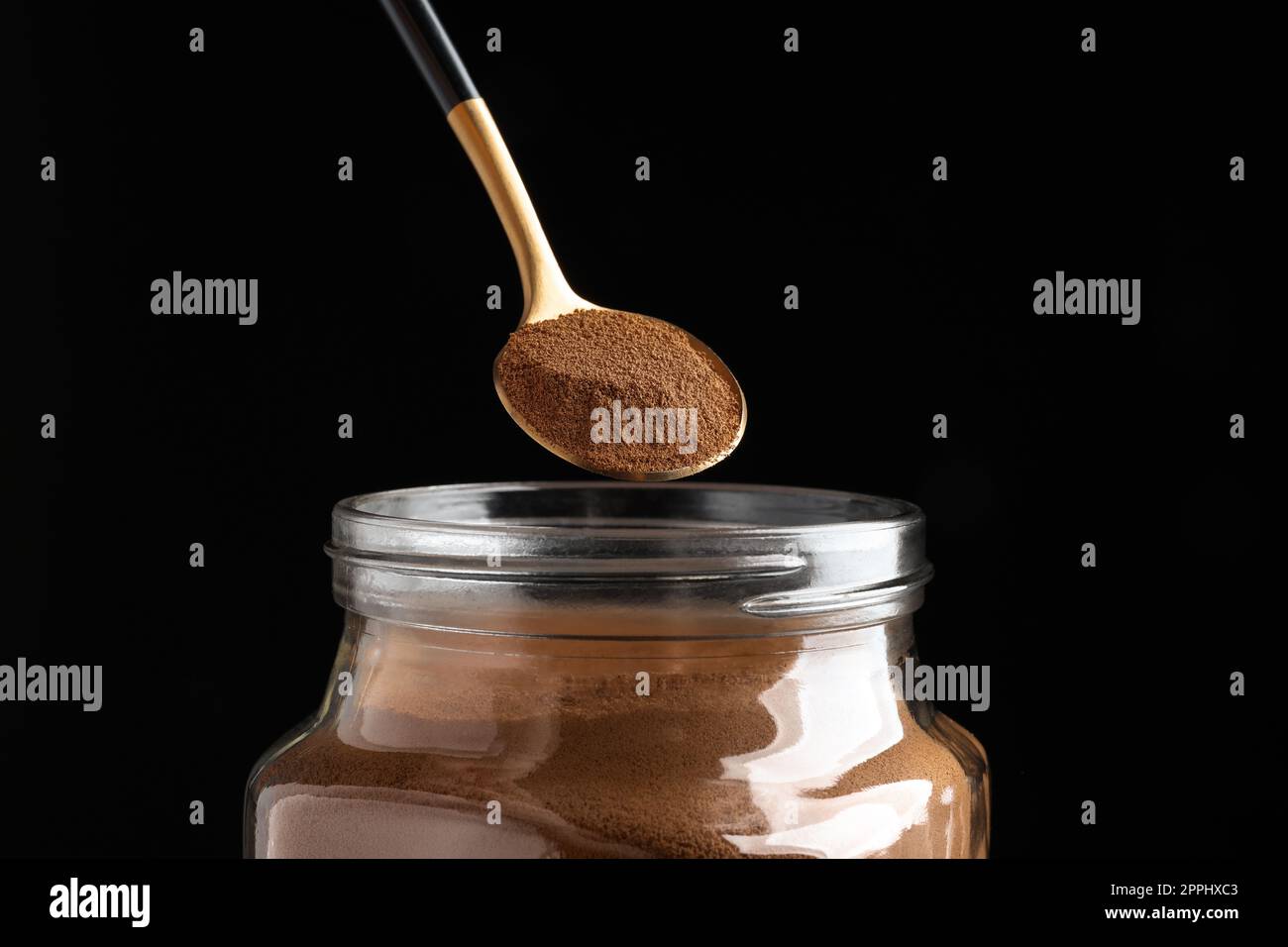 Cucchiaio di caffè istantaneo sul vaso su sfondo nero, primo piano Foto Stock