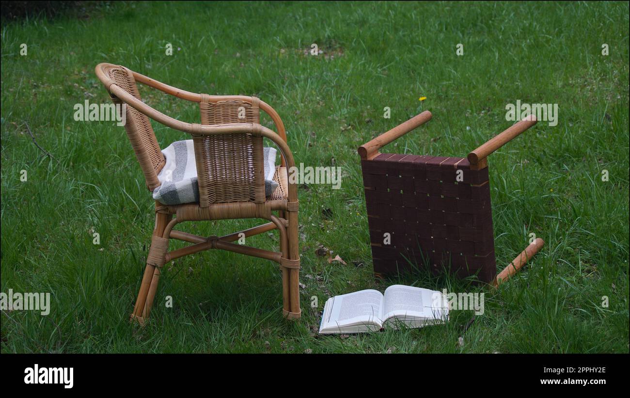 Due sedie deserte su un prato. Uno di loro cadde, con un libro che giace nell'erba. La persona che legge è andata via in fretta. Foto Stock