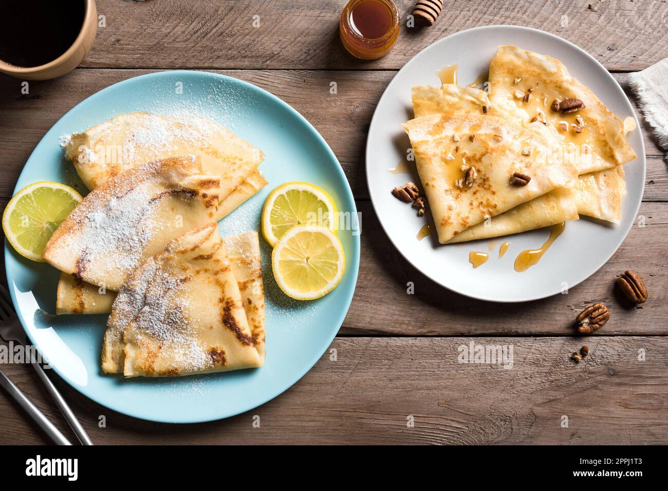 Crepes con vari condimenti - miele e noci pecan, agrumi di limone su sfondo di legno. Crepes fatti in casa per colazione o dessert. Foto Stock