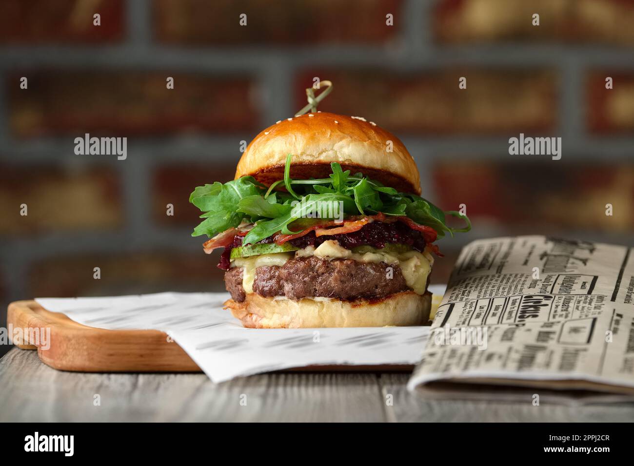 Burger sul tavolo di legno con formaggio, pancetta, pomodori vicino al giornale. Foto Stock