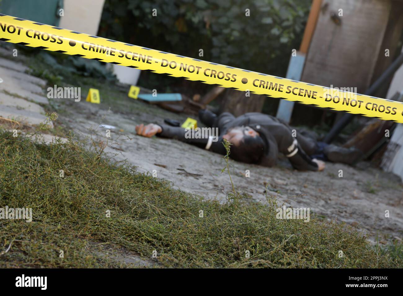 Vittima di un crimine violento in una casa residenziale di sera. Cadavere sotto la linea gialla della polizia e i segni delle prove sulla scena del crimine Foto Stock