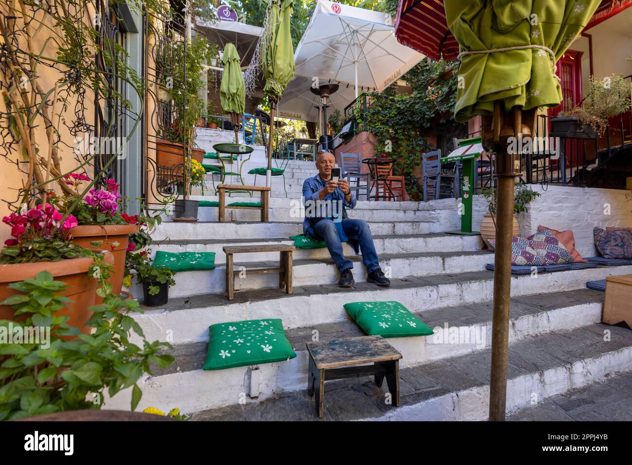 Uomo che scatta una foto con un telefono cellulare in un ristorante all'aperto sulle scale sulla strada per l'Acropoli nel quartiere Plaka, Atene, Grecia Foto Stock