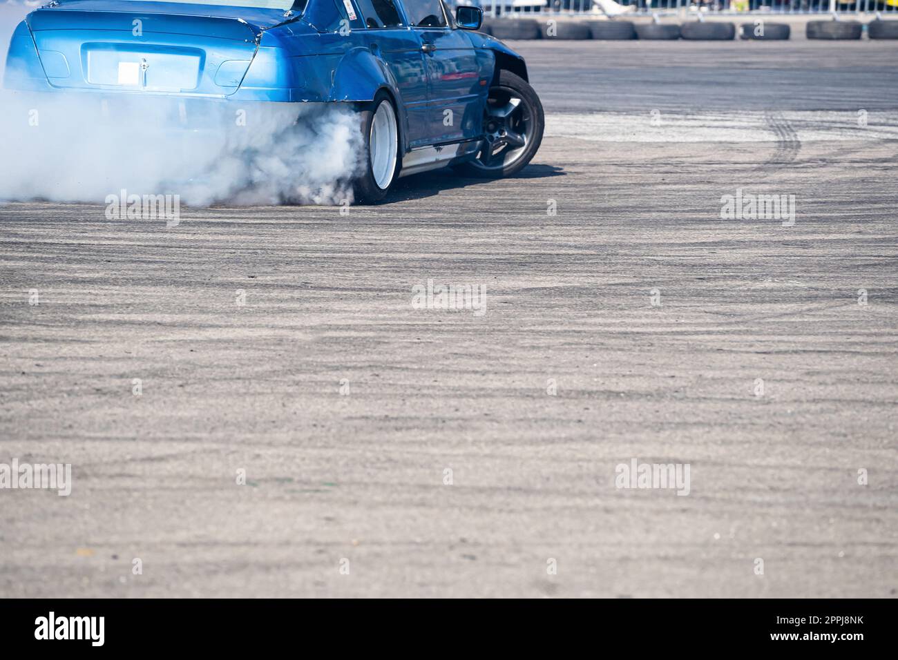 vista posteriore della vettura sportiva blu che si allontana su pista asfaltata grigia con fumo proveniente dalla ruota posteriore Foto Stock