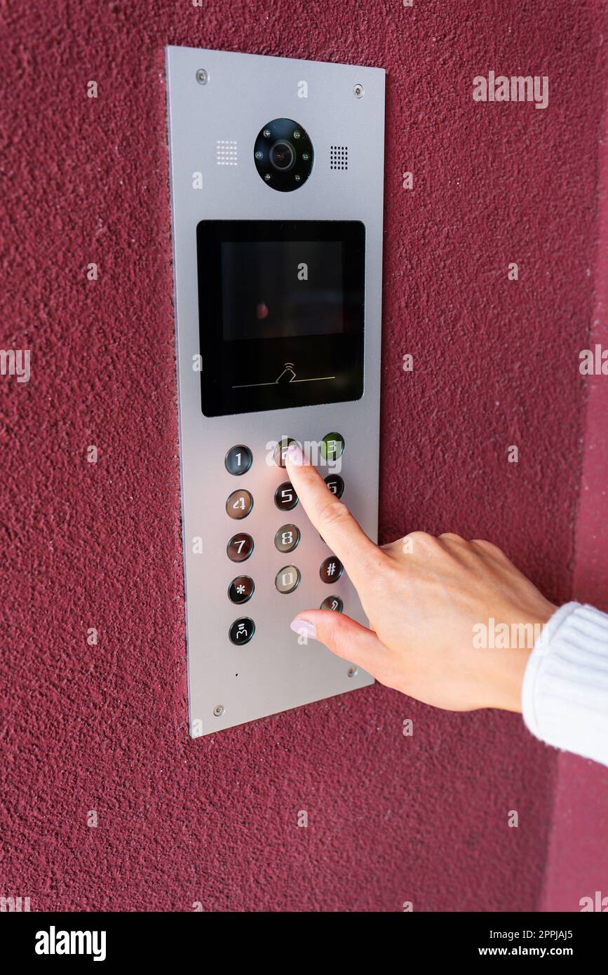 Una giovane donna compone il codice dell'appartamento sul pannello di un interfono elettronico. Concetto di protezione e sicurezza. Foto Stock