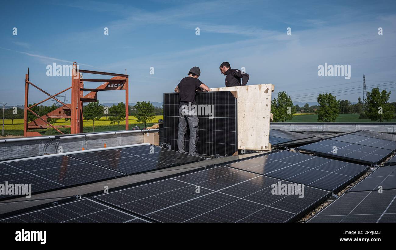 Tecnici di squadra maschi che installano un sistema di pannelli fotovoltaici solari stand-alone. Elettricisti che montano il modulo solare blu sul tetto di una casa moderna. Concetto di energia alternativa Foto Stock