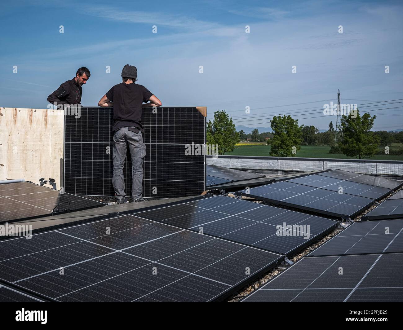 Tecnici di squadra maschi che installano un sistema di pannelli fotovoltaici solari stand-alone. Elettricisti che montano il modulo solare blu sul tetto di una casa moderna. Concetto di energia alternativa Foto Stock
