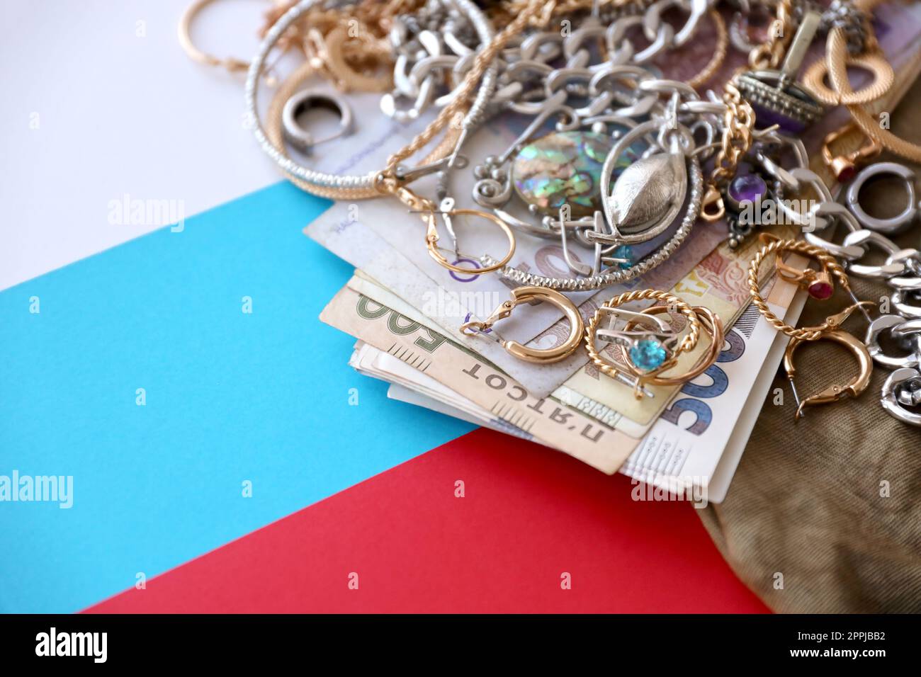 Mazzo di gioielli rubati e denaro su stoffa in uniforme militare e bandiera russa. Saccheggi da parte di soldati russi nelle città ucraine durante l'attacco russo all'Ucraina Foto Stock