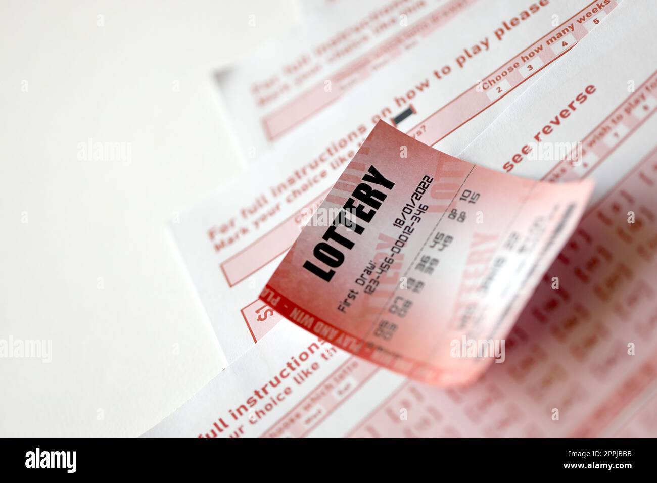 Il biglietto della lotteria rossa si trova su fogli da gioco rosa con i numeri da contrassegnare per giocare alla lotteria. Concetto di gioco alla lotteria o dipendenza dal gioco d'azzardo. Primo piano Foto Stock