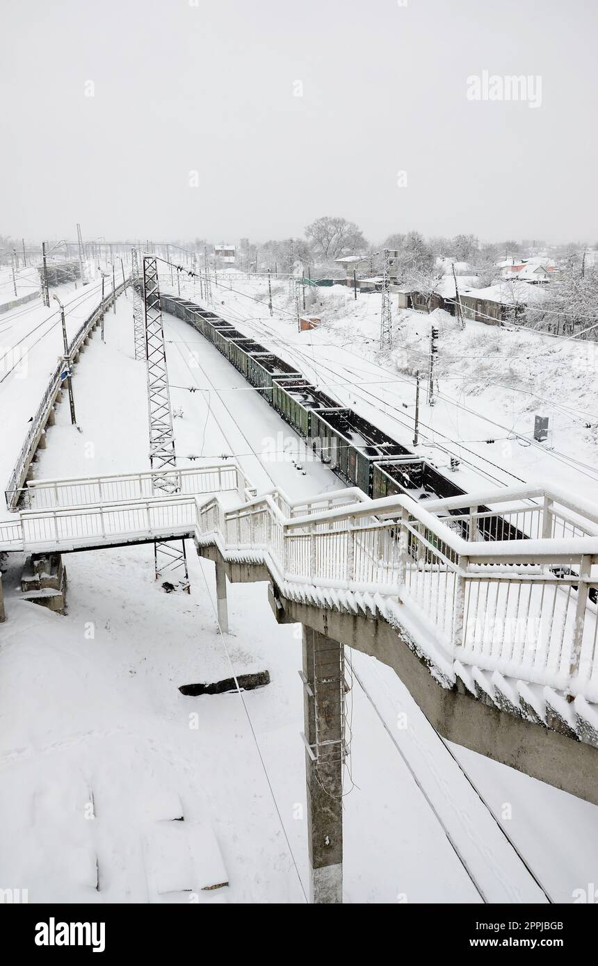 Un lungo treno di vagoni merci si muove lungo la ferrovia. Paesaggio ferroviario in inverno dopo le nevicate Foto Stock