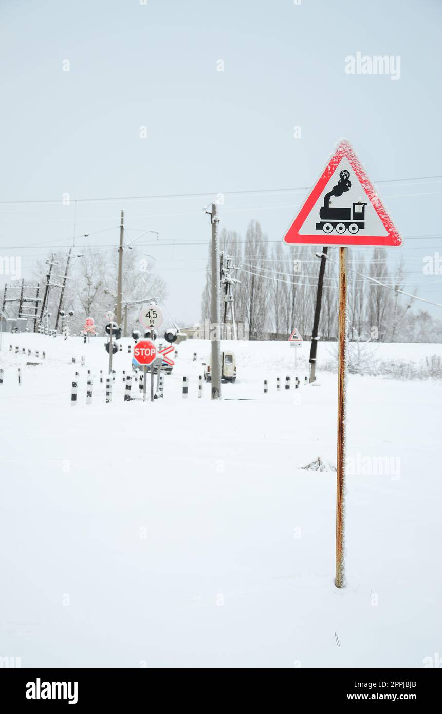 Traversata ferroviaria senza barriera con molti cartelli segnaletici nella stagione invernale innevata Foto Stock