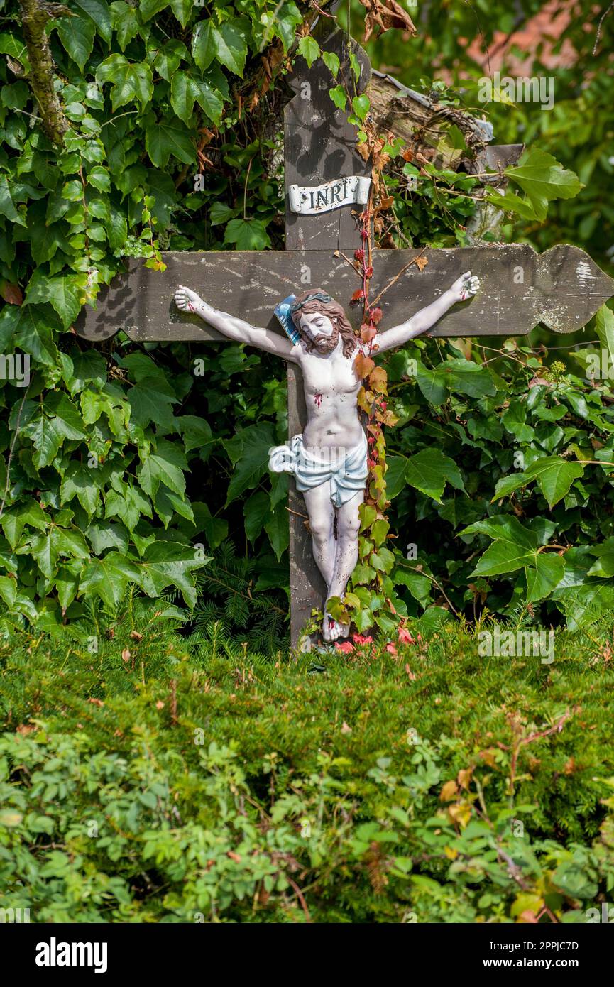 Piccola croce di legno con Gesù in mezzo verde fogliame di vari alberi Foto Stock