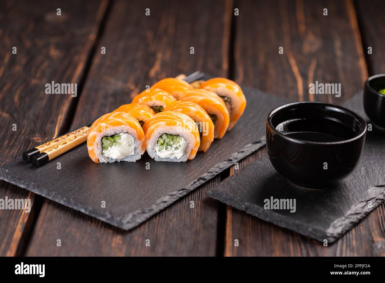 Sushi filadelfia rotolo con salmone e cetriolo e formaggio cremoso su sfondo nero. Menu sushi. Cucina giapponese Foto Stock
