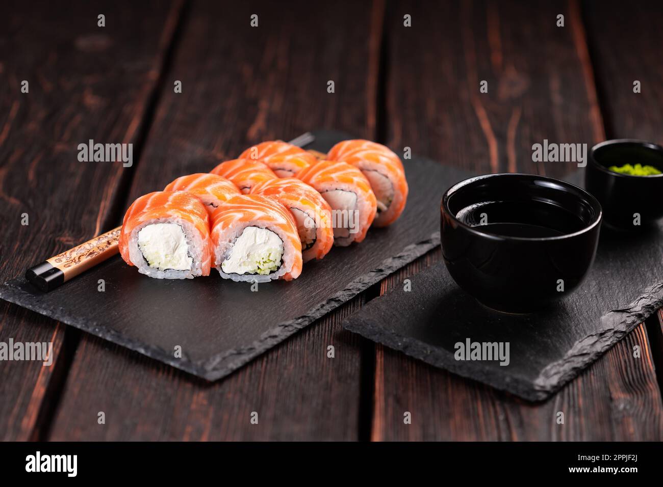 Sushi filadelfia rotolo con salmone e cetriolo e formaggio cremoso su sfondo nero. Menu sushi. Cucina giapponese Foto Stock