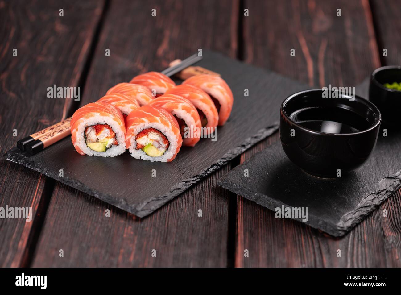 Sushi roll maguro con tonno, anguilla affumicata, avocado, Philadelphia formaggio su tavola nera. Menu sushi. Cucina giapponese. Foto Stock
