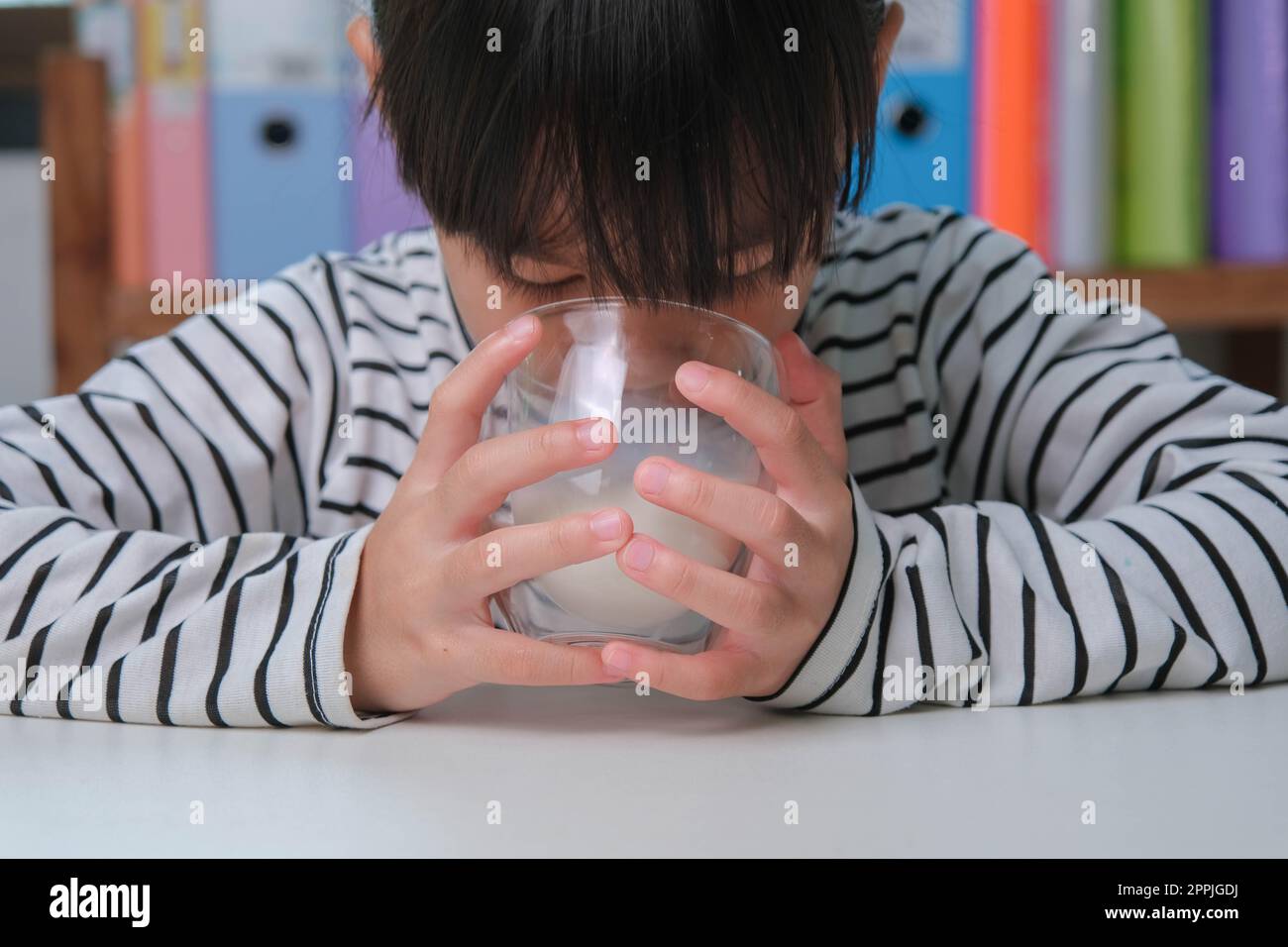 Ragazza asiatica cute che beve un bicchiere di latte a casa in soggiorno. Bambina che beve latte la mattina prima di andare a scuola. Cibo sano in chil Foto Stock
