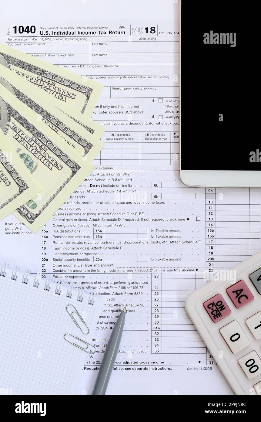Composizione delle voci che si trovano sul formulario fiscale 1040. Banconote in dollari, penna, calcolatrice, smartphone, graffetta e blocco note. Il tempo di pagare le tasse Foto Stock
