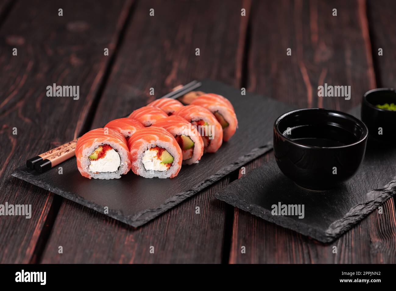 Sushi roll maguro con avocado di salmone e tobiko, Philadelphia formaggio su tavola nera primo piano. Menu sushi. Cucina giapponese. Foto Stock
