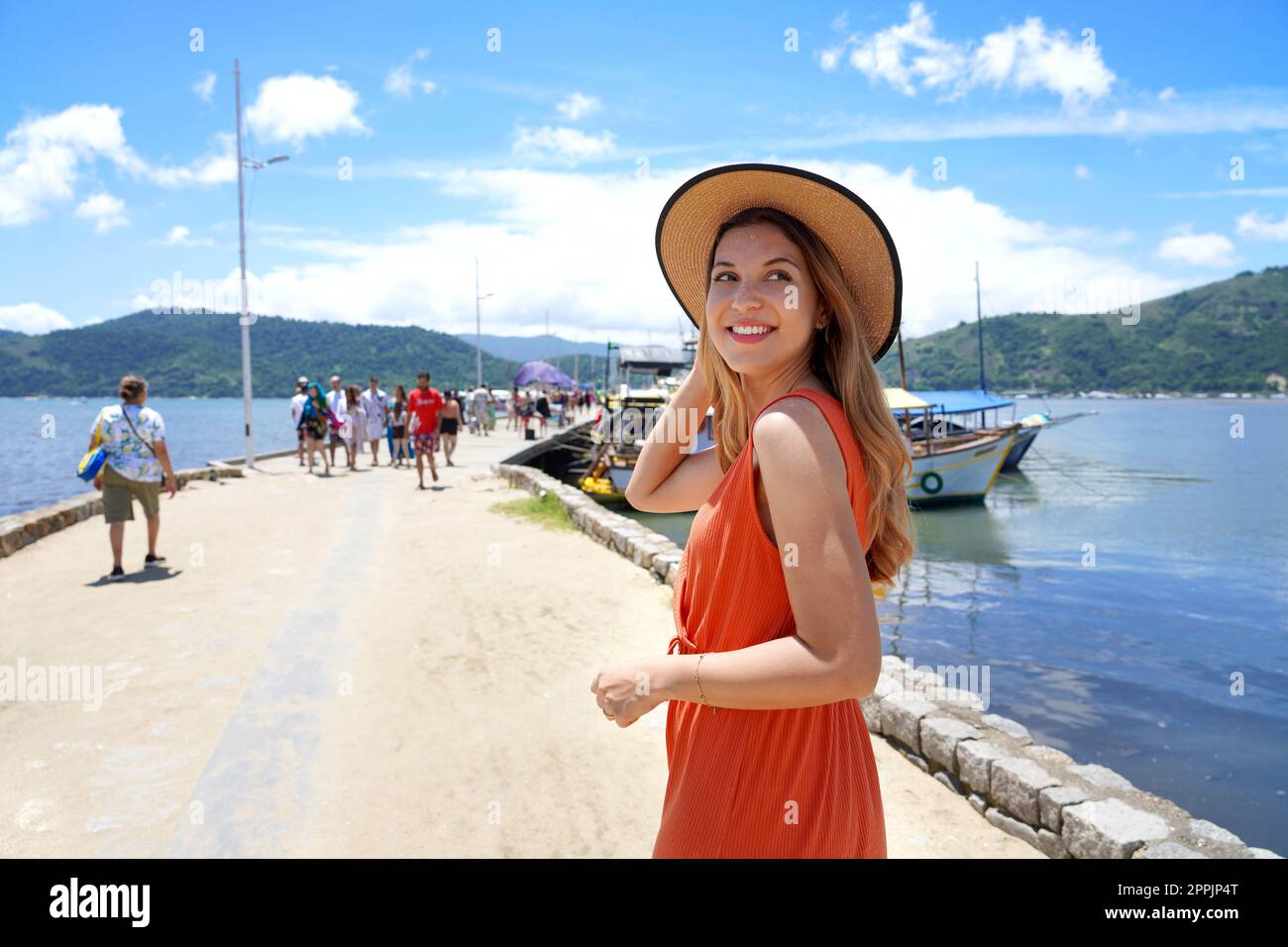 Attraente donna turistica sul molo gira intorno e guardando via sorridente pronto per il viaggio in barca in una destinazione tropicale Foto Stock