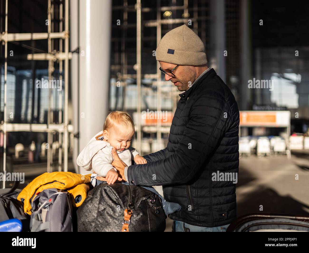 Fatherat conforta il suo bambino stanco seduto sul carrello dei bagagli di fronte alla stazione del terminal dell'aeroporto mentre viaggia con la famiglia. Foto Stock