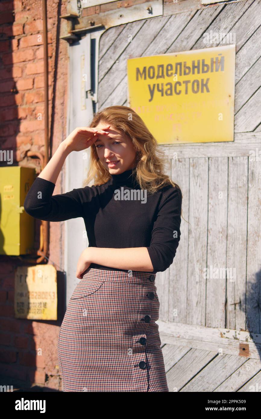 Ragazza attraente vicino alla porta della fabbrica con targhette di avvertenza che coprono gli occhi con la mano Foto Stock