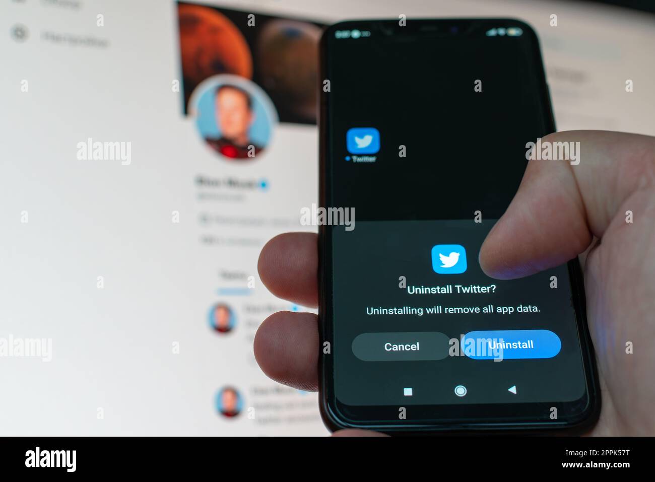 Kiev, Ucraina - 14 novembre 2022: Utente che disinstalla il social media Twitter da uno smartphone sullo sfondo del monitor con un profilo aperto di Elon Musk. Rimozione dell'app digitale a causa della dipendenza Foto Stock