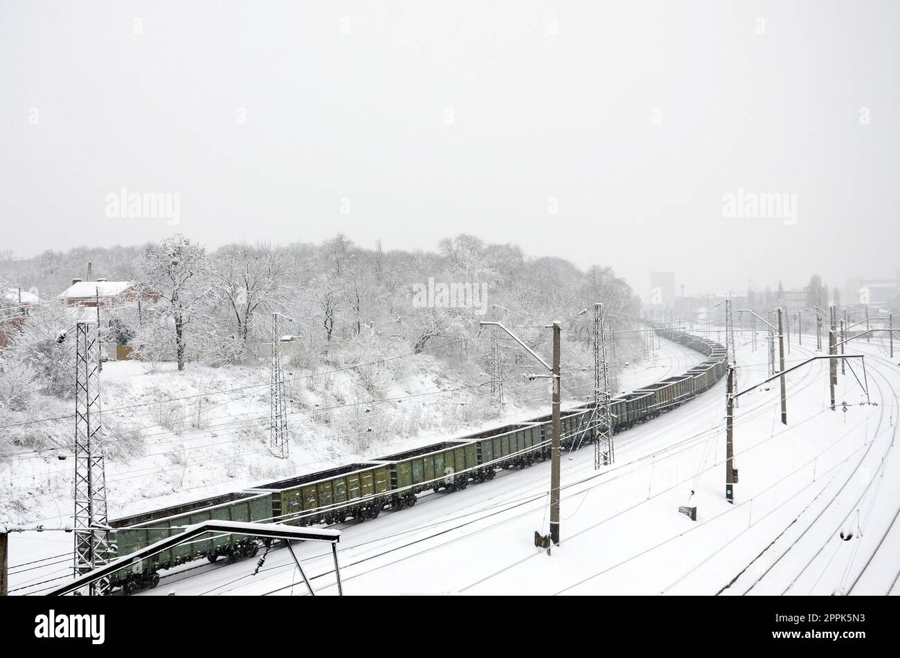 Un lungo treno di vagoni merci si muove lungo la ferrovia. Paesaggio ferroviario in inverno dopo le nevicate Foto Stock