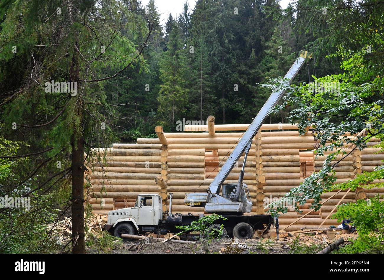 Il processo di costruzione di una casa in legno da travi di legno di forma cilindrica. La gru in condizioni di lavoro Foto Stock
